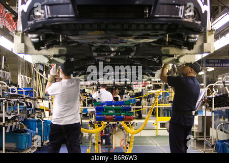 Workers at Toyota Final Assembly production line fit parts to the underside of a Toyota Avensis car Stock Photo