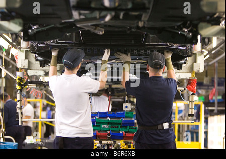 Workers at Toyota Final Assembly production line fit parts to the underside of a Toyota Avensis car Stock Photo