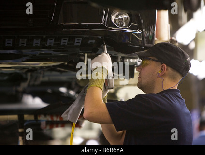 Workers at Toyota Final Assembly production line fit parts to the underside of a Toyota Avensis car Stock Photo