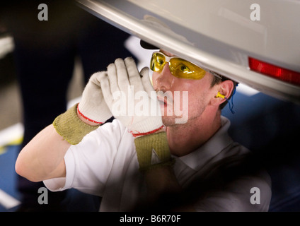 Workers at Toyota Final Assembly production line fit parts to the underside of a Toyota Avensis car Stock Photo