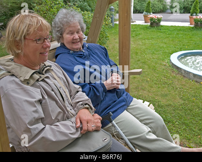 middleaged woman visiting her mother in home for old people sitting in garden having a chat Stock Photo