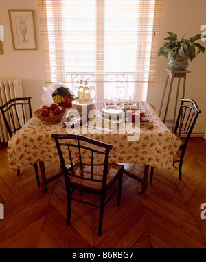 Antique chairs at table with quilted table cloth in front of French windows in townhouse dining room with parquet flooring Stock Photo