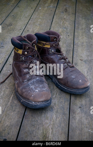 A pair of old brown leather Caterpillar walking boots on a wooden floor tough as old boots Stock Photo