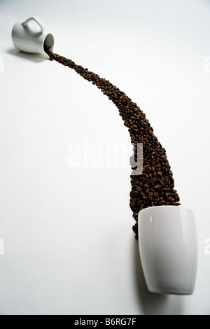 Coffee beans poured from a pitcher to a coffee cup. Stock Photo