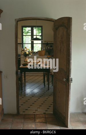 View from hall through open door to country kitchen with pottery bowls on wooden table in front of window Stock Photo
