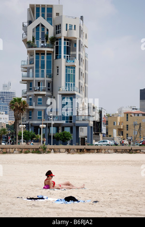 Israel Tel Aviv a woman sunbathing on the beach a modern building on Trumpeldor street in the background Stock Photo