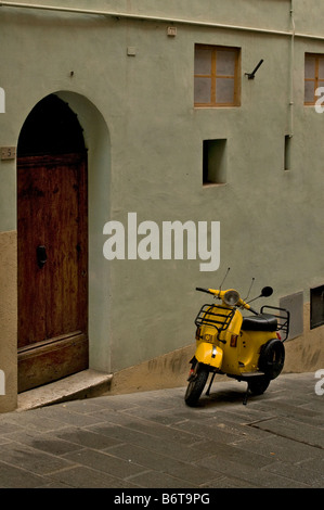 Bright yellow scooter parked against green walled building in Sienna Italy with little square window and wooden arched door Stock Photo