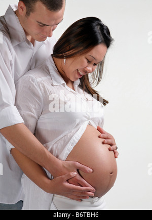 happy young bi-racial couple cradling large pregnant womb together Stock Photo