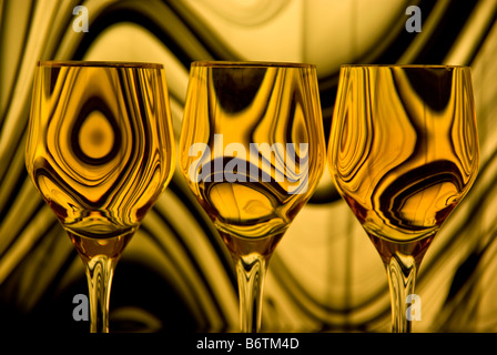 Close up of three wine glasses with a background of gold and black swirling lines reflected in each glass. Stock Photo