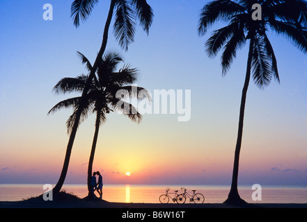 Couple embracing at beach, sunrise with palm trees, bicycles, Miami Stock Photo