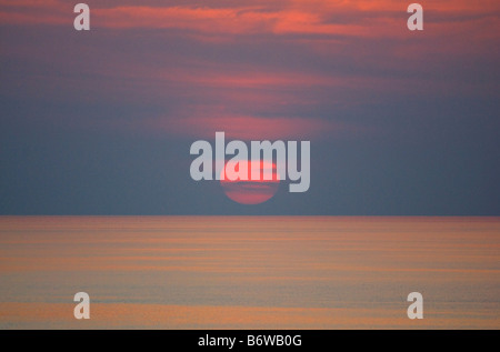 LARGE RED SUN SETTING ON SEA WITH CLOUDS Stock Photo