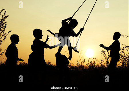 Silhouette of Indian children playing on a home made swing in the countryside at sunset. Andhra Pradesh, India Stock Photo