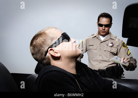 Police officer holding pack of drugs by man seated in car Stock Photo