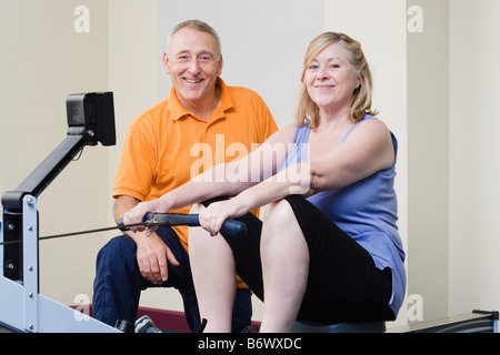 Personal trainer helping a woman on a rowing machine Stock Photo