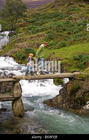 Wales, Conwy, Snowdonia. Man leads a boy across a rustic bridge over the Afon Cwm Llan on the route into Snowdon Stock Photo