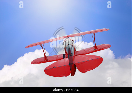 A red biplane flying high above the clouds towards the sun Stock Photo