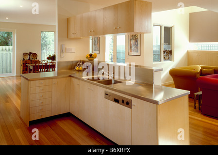 Stainless steel worktops and fitted dishwasher in openplan kitchen with pale wood units and view of living room and dining room Stock Photo