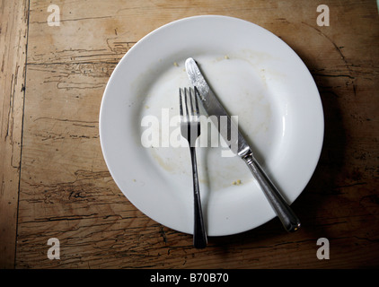 Knife and Fork on an empty plate on a wooden table. Stock Photo