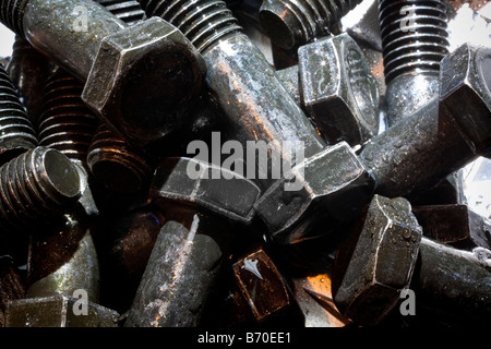 Random  artistic pile of threaded bolts on a sheet steel, backlit. Stock Photo