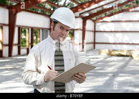 A construction inspector in a steel frame building making notes and looking suspicious Stock Photo