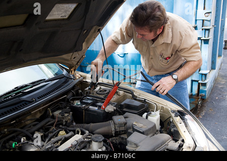 Auto mechanic using jumper cables to charge a car battery Stock Photo