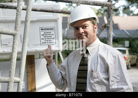 A building inspector standing under scaffolding pointing out the WARNING sign posted on the jobsite Stock Photo