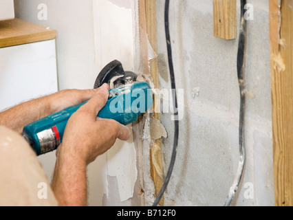 Contractor using an angle grinder to cut drywall White specs in image are construction dust not noise Authentic and accurate con Stock Photo