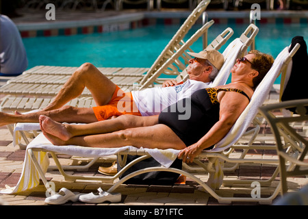 Palm Beach Shores mature middle aged large lady in swimming costume on sun lounger sunbathing by pool with husband in shorts Stock Photo