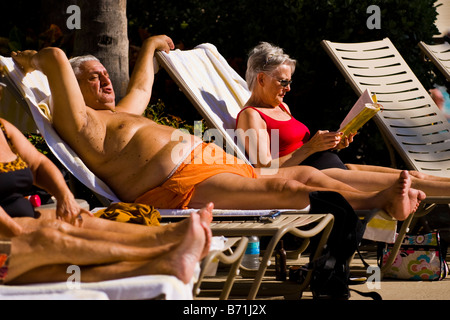 Palm Beach Shores , mature large middle aged grey haired man on sun lounger in orange swimming costume sunbathes by pool Stock Photo
