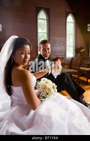 Young interracial bride and groom sitting on wooden altar of church on wedding day Stock Photo