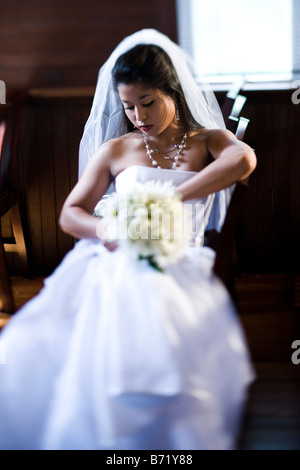 Young bride sitting in church holding bouquet on wedding day Stock Photo