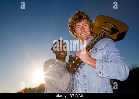 Young interracial couple standing with guitar on beach Stock Photo
