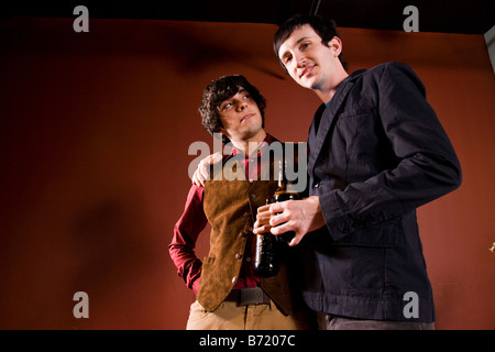 Two stylish young men standing with arms around one another holding drinks Stock Photo
