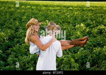 Young man carrying young woman in field wearing cowboy hat Stock Photo