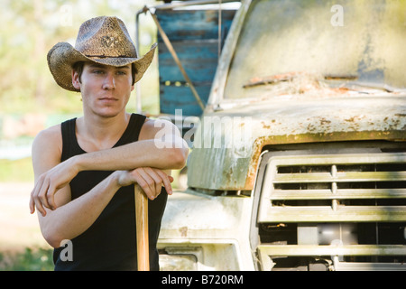 Young man standing by truck holding shovel wearing cowboy hat Stock Photo