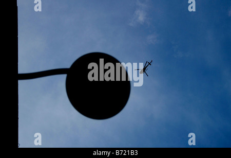 A helicopter flies high above a silhouetted lamp post in Boston Mass Stock Photo