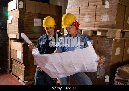 Two workers standing in storage warehouse looking at plans Stock Photo
