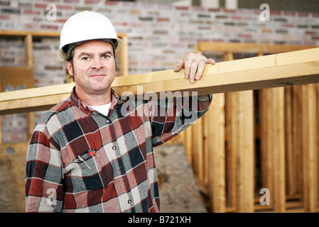 A construction day laborer carrying wood beams Authentic construction worker on an actual construciton site Stock Photo