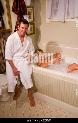Woman relaxing in a bubble bath with man sitting on bathtub Stock Photo