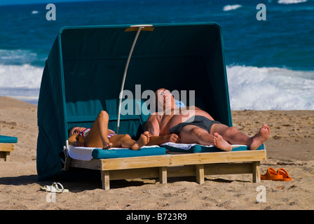 Palm Beach Shores , middle aged couple in swim suits sunbathing on sunny day under cabana canopy on loungers by the sea shore Stock Photo