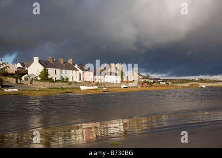 View across tidal Afon Ffraw River to village with dark clouds in dramatic sky on west coast. Aberffraw Isle of Anglesey North Wales UK Stock Photo