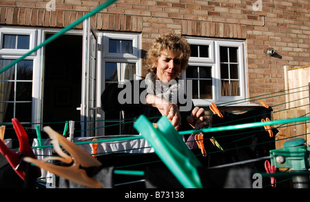 Blonde middle aged woman pegging clothes to a washing line on a cold winter morning Stock Photo