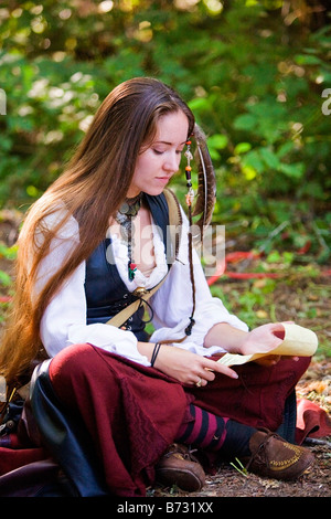 Image of a young woman dressed in Medieval clothing sitting on the ground reading what appears to be a note Stock Photo