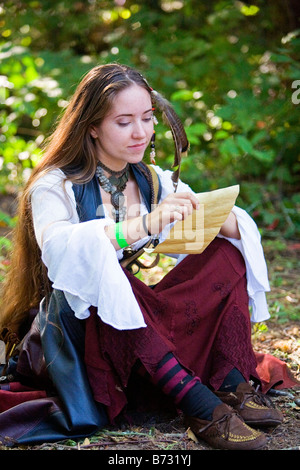 Image of a young woman dressed in Medieval clothing sitting on the ground reading what appears to be a note Stock Photo