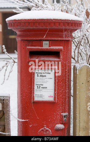 A traditional iconic red Royal Mail letter post box is pictured on a cold snowy winters day in the UK Stock Photo