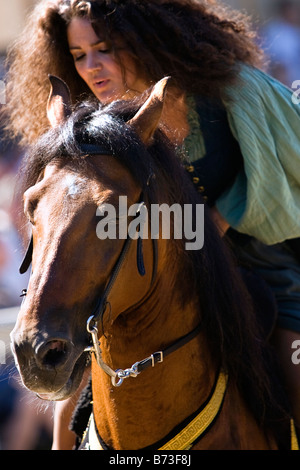 Image of a young woman dressed in Medieval clothing sitting on a horse whispering to it calming it down Stock Photo