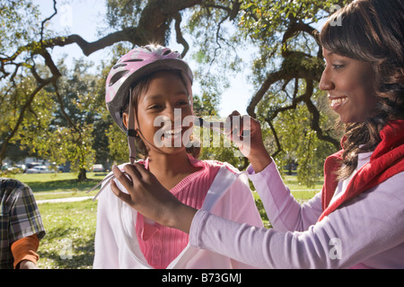 African American mother fastening bike helmet on girl in park Stock Photo