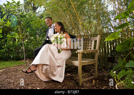 Happy African-American bride and groom on bench outdoors on wedding day Stock Photo