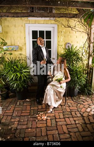 African-American bride and groom laughing, drinking champagne on patio Stock Photo