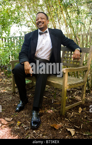 Happy African-American man wearing tuxedo sitting on bench Stock Photo